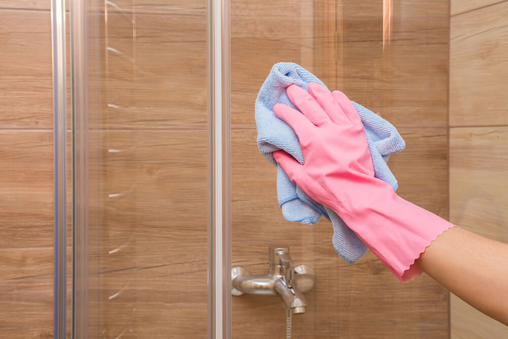 Housewife washing and polishing a glass shower door