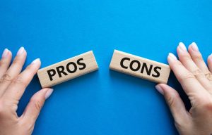 Hand holding blocks that read pros and cons on a blue background